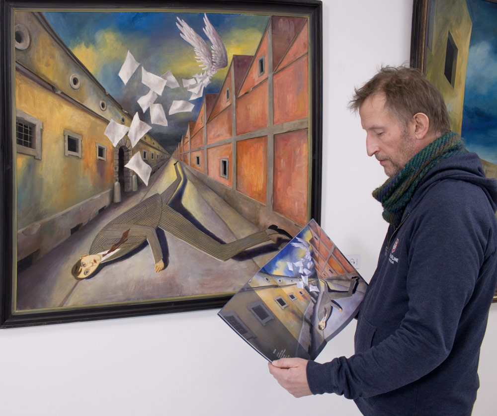Heitz Ratz mit dem Katalog zur Sonderausstellung „Sein Name ist Zeiger“ vor dem Bild „Die Flucht II“ von Wolfgang Lettl.